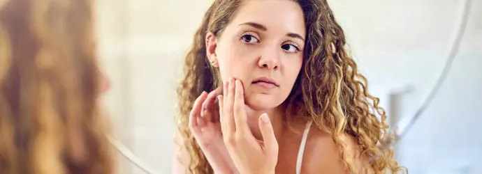 A young woman squeezing a pimple on her oily skin and looking at the mirror