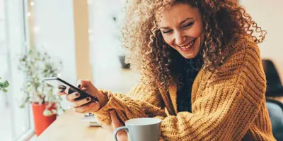 a lady with curly hair smiling at her mobile phone