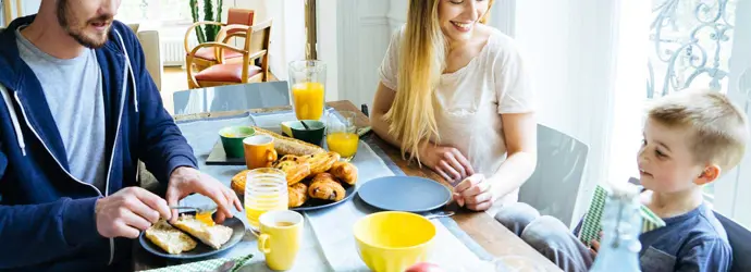 A family of three sitting around a table having breakfast in the morning