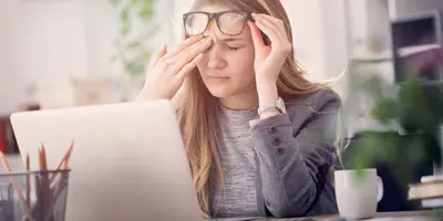 Young woman suffering from eye strain while working on a laptop which is one of the causes of watery eyes