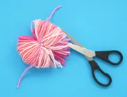 Black scissors used to cut the outer ends of the loop into strands, all still secured by the central pink wool string.