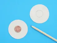 Two cardboard cutout circles laid on a blue surface with a coin in the centre of one and a pencil on the side.