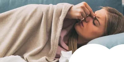 Woman lying on the sofa holding her nose, surrounded by tissues