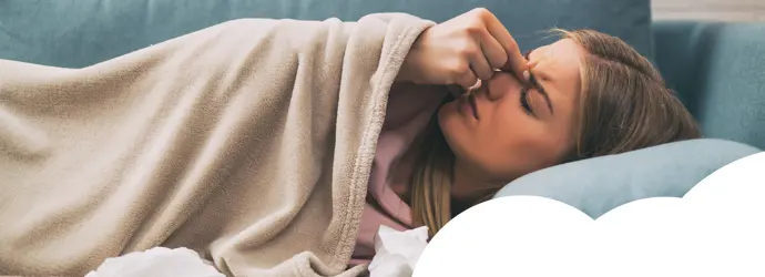 Woman lying on the sofa holding her nose, surrounded by tissues