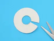 A cardboard cutout of a thick ring with a thin wedge cut and a pair of scissors on the side.