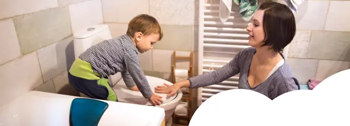 Little boy puts the toilet seat lid down with help from his mother.