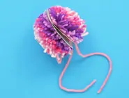 A pink wollen pom pom with cardboard in the centre, tied together with a pink wool string. A pink wollen pom pom with cardboard in the centre, tied together with a pink wool string.